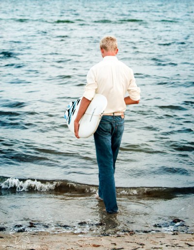 boy fully dressed walking into water with surfboard