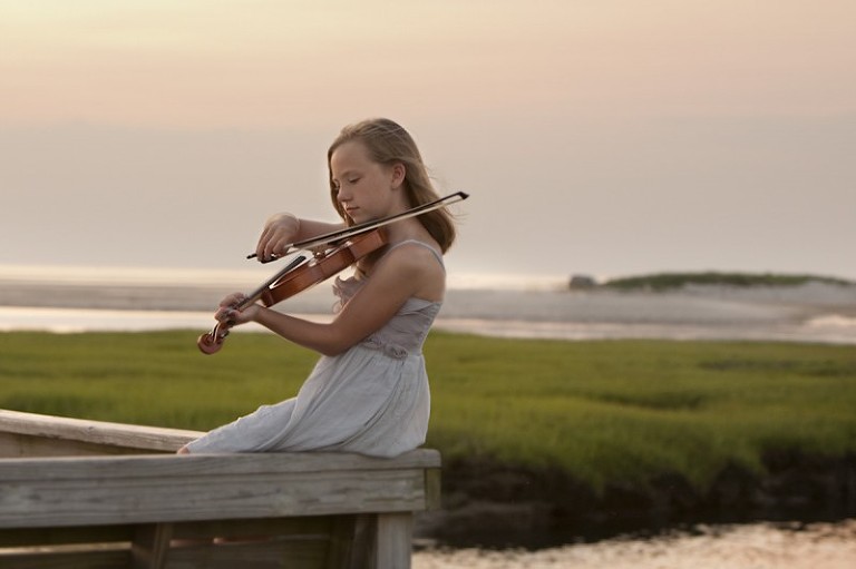 Young girl playing violin by the ocean