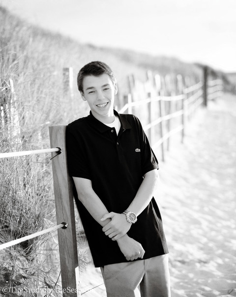 Teen boy by beach fence black and white