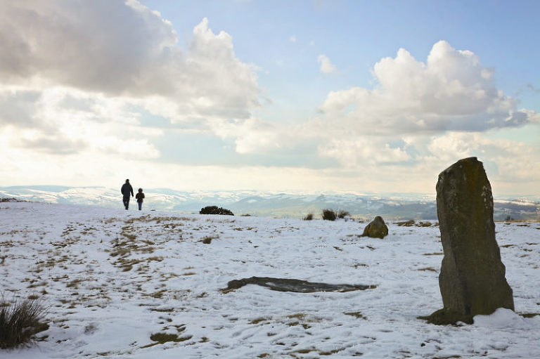 dad and daughter walking on snowy day near standing stones