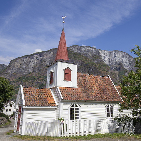 small white wooden stave church with mountains behind