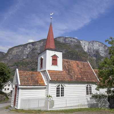 small white wooden stave church with mountains behind