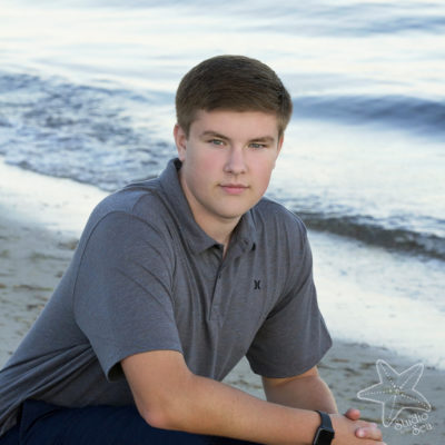 Square photo of senior boy kneeling in front of ocean