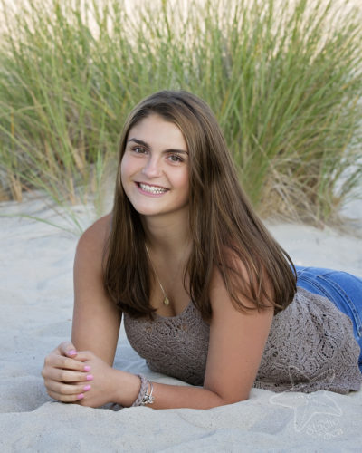 Senior girl lying on tummy in sand with a lovely smile