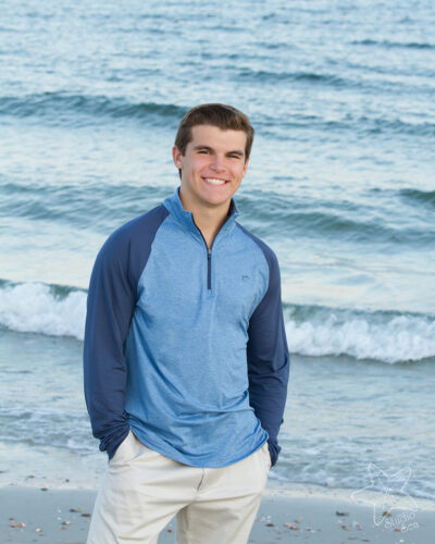 Senior boy in blue shep standing in front of very blue ocean