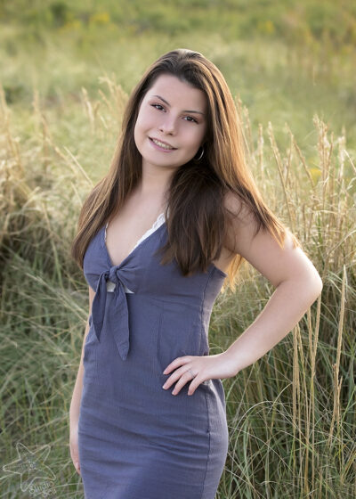 Brown haired girl back lit in front of beach grass