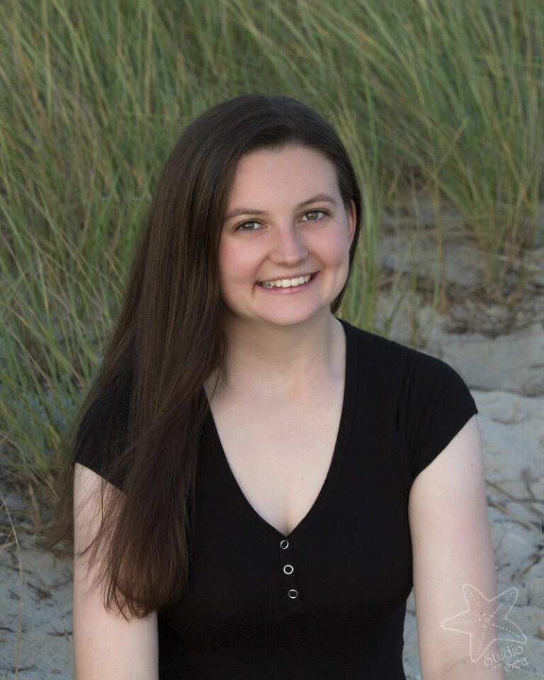 brunette senior girl smiling in front of beach grass